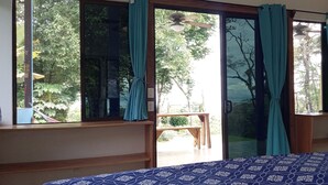 Une chambre avec un lit, une fenêtre avec des rideaux, un ventilateur de plafond et une vue sur l’extérieur.