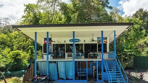 Un bâtiment à deux étages doté d’un patio couvert, d’un escalier et d’une moto garée à l’extérieur.