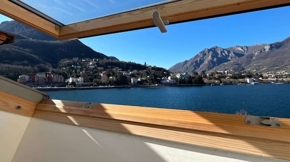 Une vue depuis un bateau ou une cabane dotée d’une rambarde en bois, donnant sur un lac avec une ville et des montagnes en arrière-plan.