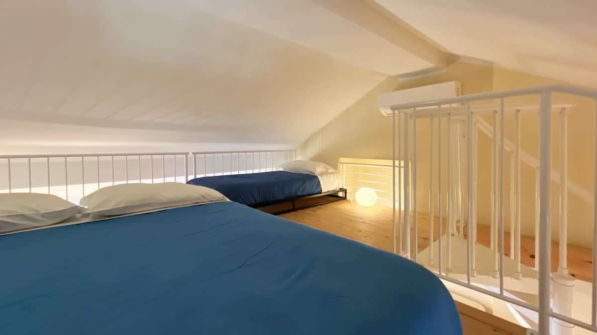 A dormitory room with two beds, a staircase, and a white railing.