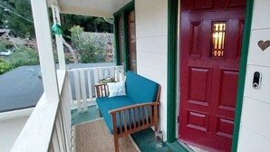 Un porche avec une porte rouge, un banc et une boîte aux lettres.