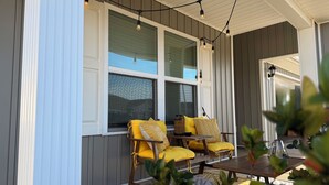 Eine überdachte Veranda mit zwei Holzstühlen und einem Tisch, ausgestattet mit großen Fenstern und Lichterketten.