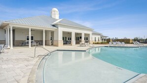 Ein Poolbereich mit überdachter Terrasse, Liegestühlen und einem Gebäude mit weißer Fassade und Schornstein.