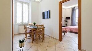 A room with a dining area featuring a wooden table and chairs, a potted plant, and a window with sheer curtains. - Whiteten Rome Apartment (Roma)