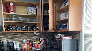 Une cuisine compacte dotée de meubles en bois, d’un four à micro-ondes, d’une machine à café et de divers produits alimentaires.