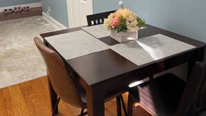 Un coin repas avec une table en bois foncé, deux chaises, un vase de fleurs et un téléviseur fixé au mur.