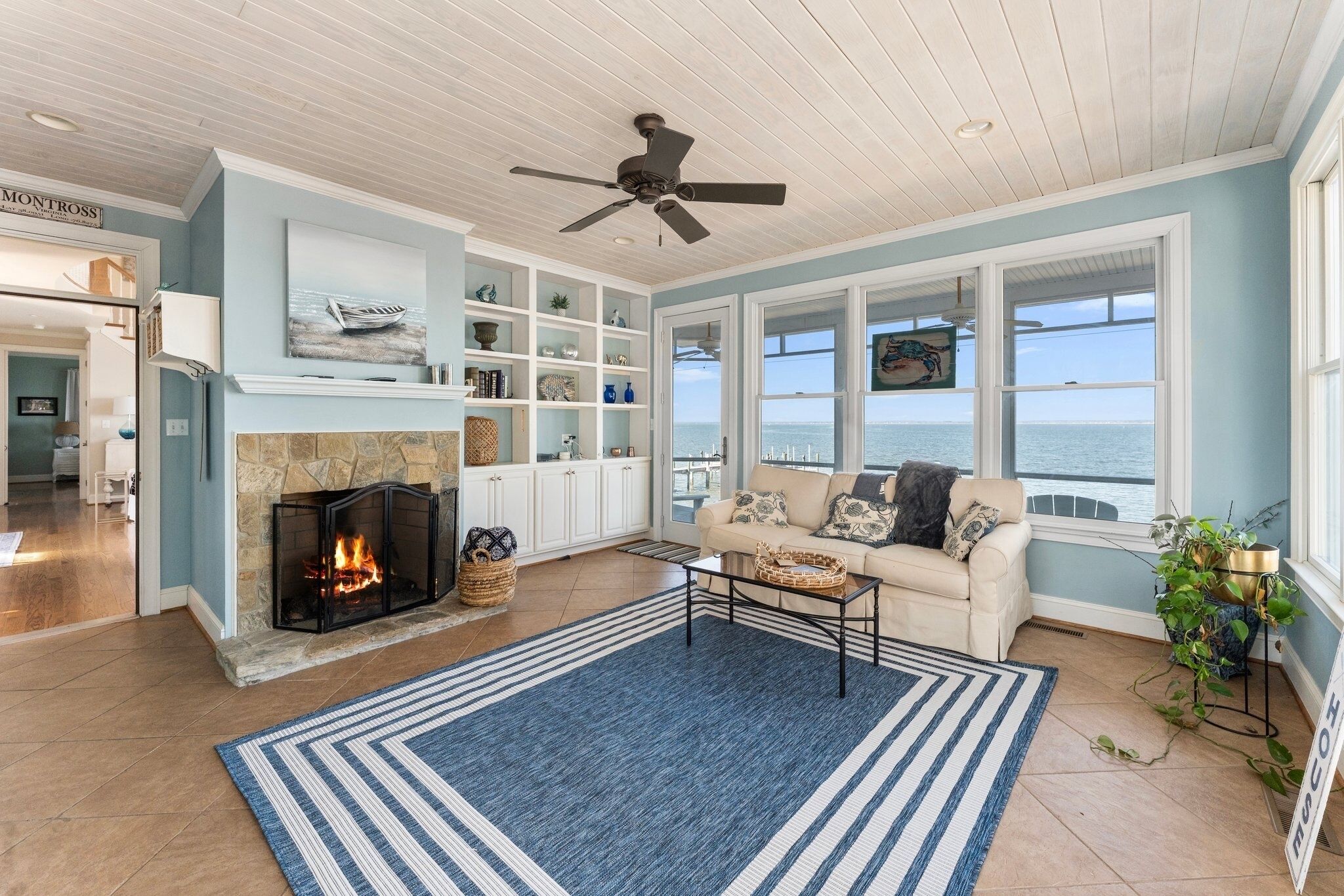 A living room with a fireplace, a ceiling fan, and a view of the ocean.