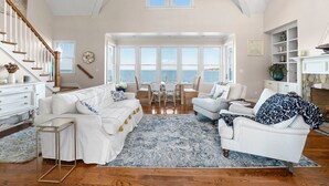 A spacious living room with a view of the sea, a white staircase, and a fireplace.