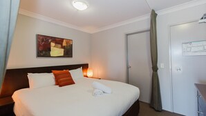 A hotel room with a bed, a painting on the wall, a nightstand, a lamp, and an emergency exit sign. - Horizons - 418/10 Kosciuszko Road (Jindabyne)