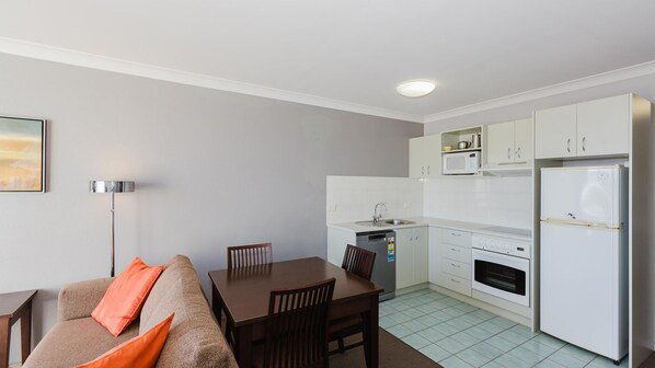 Un espacio habitable compacto con kitchenette, comedor y sofá con cojines naranja.