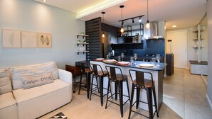 A modern kitchen with a central island, bar stools, and a dining area. - Studio Shopping OKA Floripa - Campeche - SOK125 (Florianópolis)