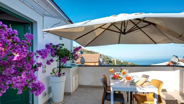 Un balcon avec une table dressée pour deux personnes, une plante en pot et une vue sur la mer.