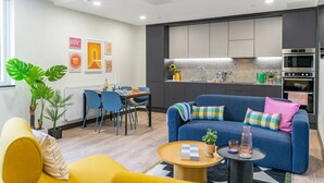 A modern living room with a blue sofa, yellow armchair, and a dining area with blue chairs. - The Residence Dublin (Dublin)