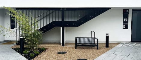 A modern building exterior with a staircase, a bench, and a small garden area.
