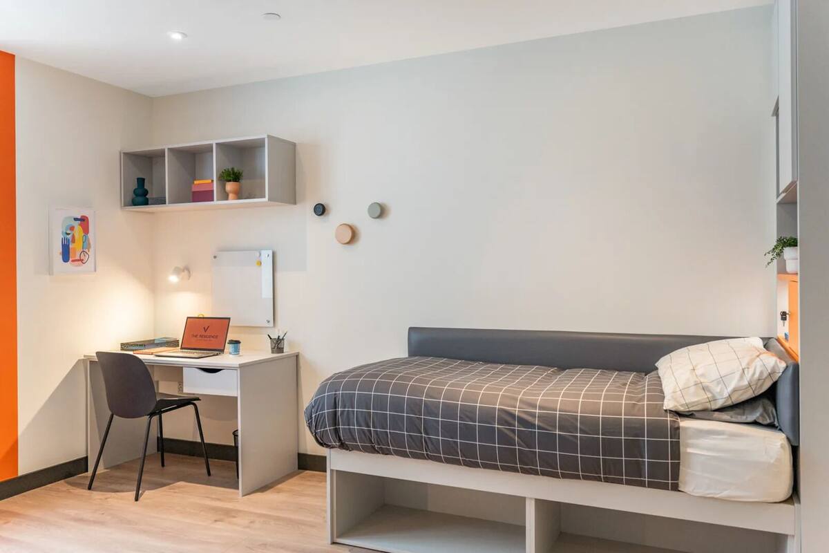 Een kleine slaapkamer met een bed, een bureau en een stoel.
