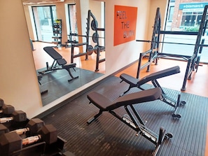 Een fitnessruimte met gewichthefapparatuur, banken en een spiegel die de ruimte weerspiegelt.