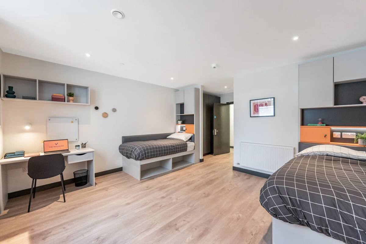 Een moderne slaapkamer met een bed, een bureau en een stoel. Er is een whiteboard aan de muur en een plank met decoratieve objecten.
