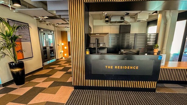 A reception desk with a sign reading "THE RESIDENCE" in a modern lobby with geometric patterned flooring and a potted plant. - The Residence Dublin (Dublin)