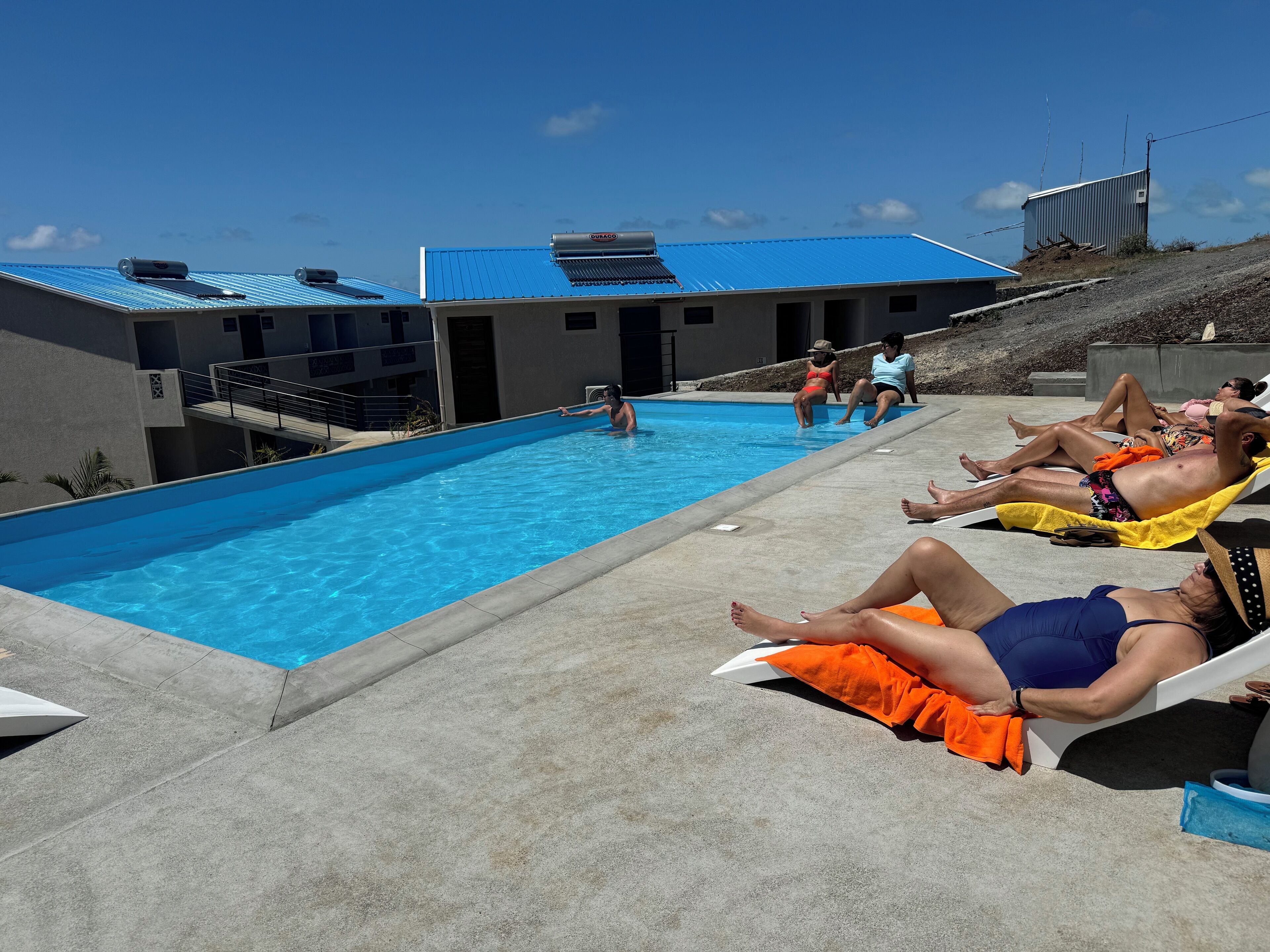 Zona de piscina con sillas de descanso y un edificio con techo azul.