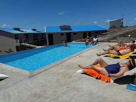Zona de piscina con sillas de descanso y un edificio con techo azul.