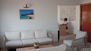 Un salon moderne comprenant un canapé, deux fauteuils, une table basse en bois avec une plante, un bureau avec un ordinateur portable et un tableau représentant un paysage côtier.