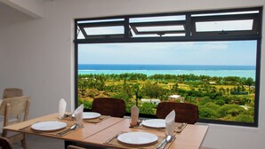 Un coin repas avec une table dressée pour quatre personnes, donnant sur un paysage côtier avec vue sur la mer et la végétation.
