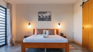 Une chambre d’hôtel avec un lit en bois, deux tables de chevet, un tableau accroché au mur et une porte coulissante.