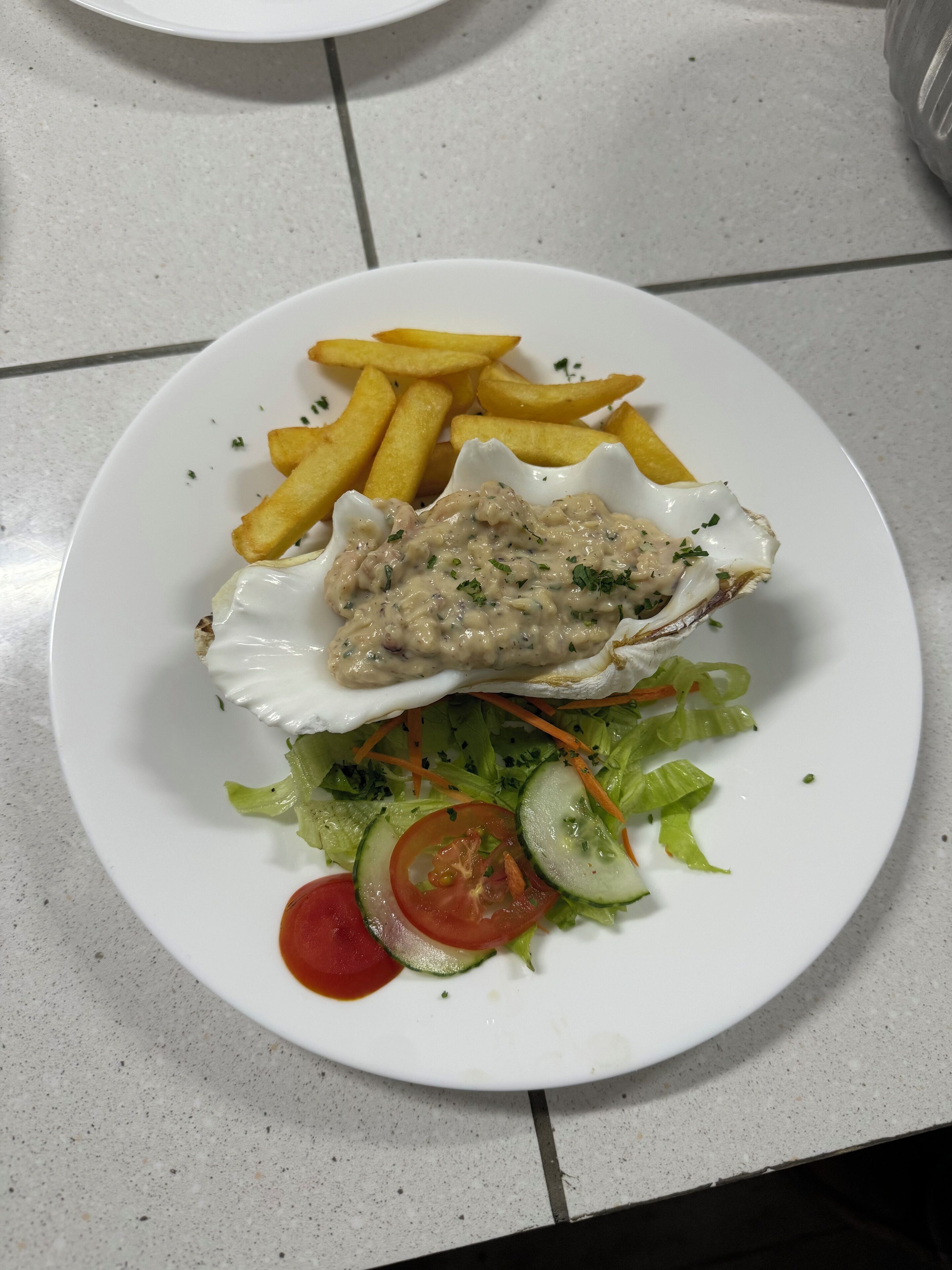 Une assiette contenant une salade, une tranche de tomate, des concombres et de la laitue, le tout nappé d’une sauce crémeuse et accompagné d’un morceau de poisson.