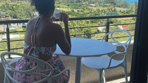 Une personne assise à une table, avec vue sur l’océan et la végétation.