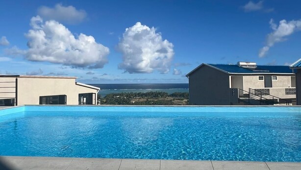 Une piscine offrant une vue dégagée sur l’océan et, en arrière-plan, un bâtiment surmonté d’un toit bleu.