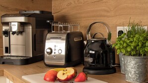 A kitchen counter with a coffee maker, toaster, kettle, and a cutting board with apples and strawberries.