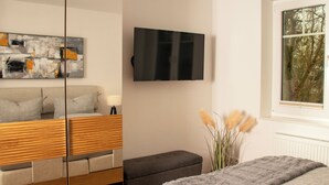 A modern bedroom with a sofa, a flat-screen TV, a window with a view, and a decorative plant.