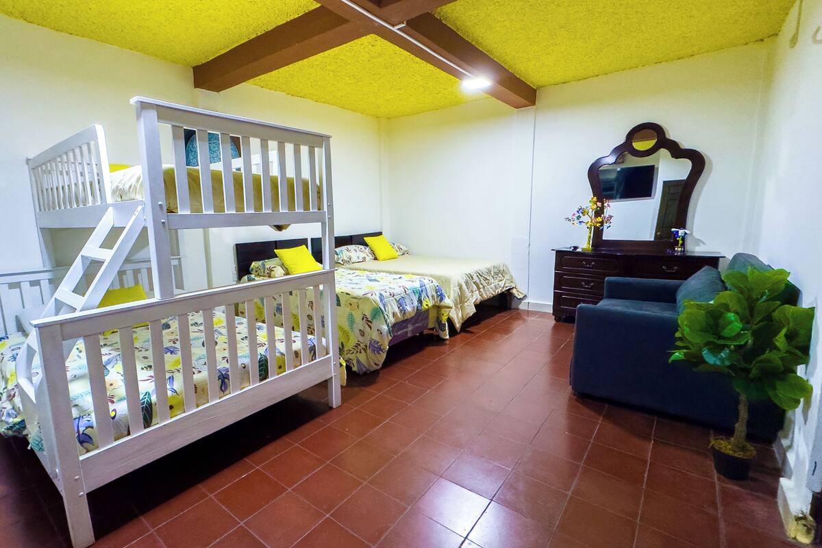 Een kamer met een stapelbed, een eenpersoonsbed, een dressoir, een spiegel en een potplant.