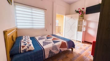 Un dormitorio con cama, ventana con persianas, armario y televisor en la pared.