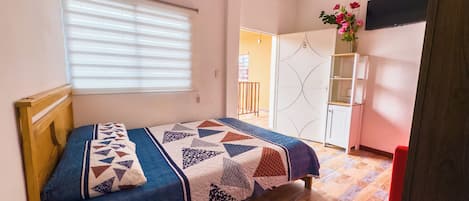 Un dormitorio con cama, ventana con persianas, armario y televisor en la pared.