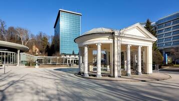 Un pabellón con columnas, un edificio moderno al fondo y un cielo despejado.