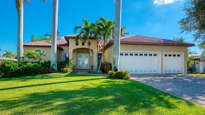 A two-story house with a red-tiled roof, a front entrance with a door, and a garage with two doors. - VRCC Villa Poseidon’s Paradise (Cape Coral)