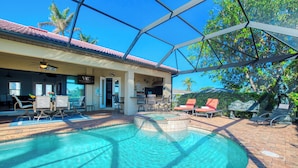 A pool area with a covered patio, outdoor seating, and a view of the surrounding landscape. - VRCC Villa Poseidon’s Paradise (Cape Coral)