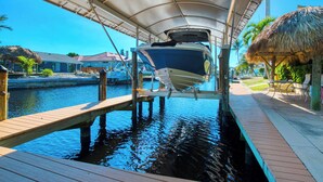 A boat docked under a covered area with a wooden deck and a thatched-roof structure nearby. - VRCC Villa Poseidon’s Paradise (Cape Coral)