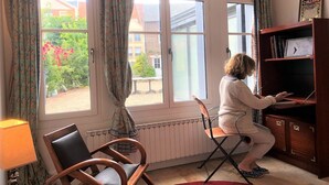 Une pièce avec une fenêtre, un radiateur, une chaise en bois, un tapis rouge et une bibliothèque.
