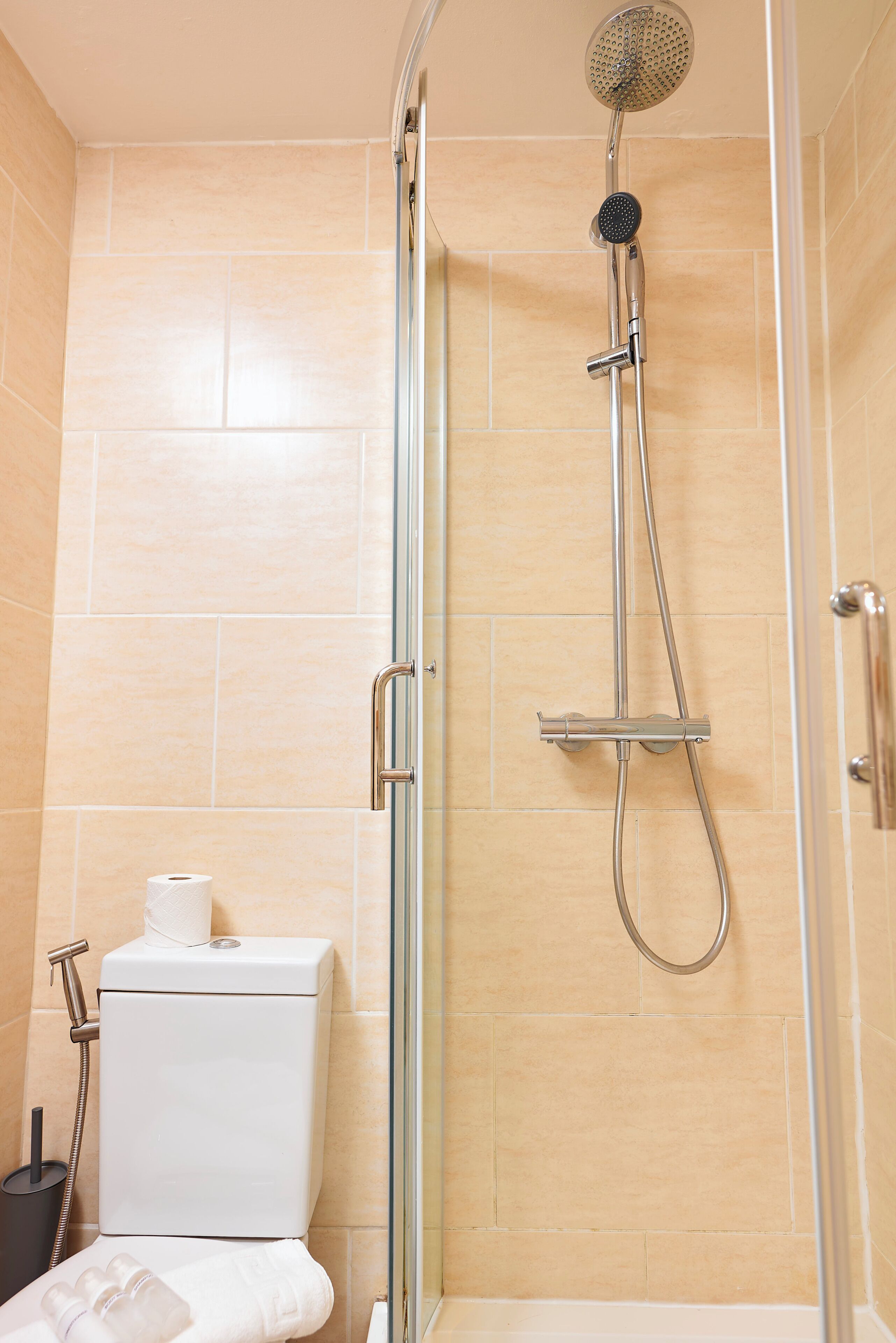 Eine Dusche mit Duschbrause, Glaswand und Toilette mit Toilettenpapier.