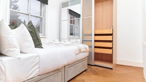 A bedroom with a bed, a window, a wardrobe, and a small table with towels. - Chic 1-Bed Flat w/Terrace in Notting Hill W10 (London)