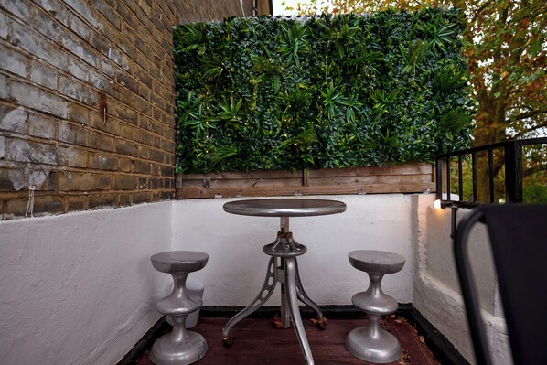 A small outdoor seating area with a brick wall, a green vertical garden, and a metal table with two stools.
