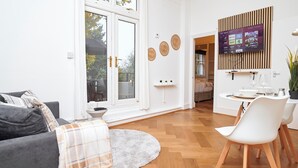 A modern living room with a grey sofa, a round rug, a dining area with a white table and chairs, and a TV mounted on a wooden panel wall. - Chic 1-Bed Flat w/Terrace in Notting Hill W10 (London)