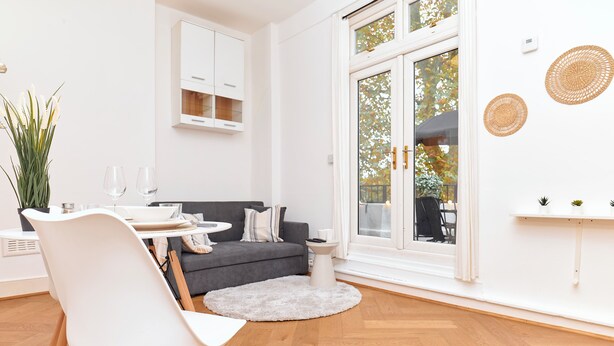 A modern living room with a white chair, a grey sofa, a round coffee table, and a white cabinet. - Chic 1-Bed Flat w/Terrace in Notting Hill W10 (London)