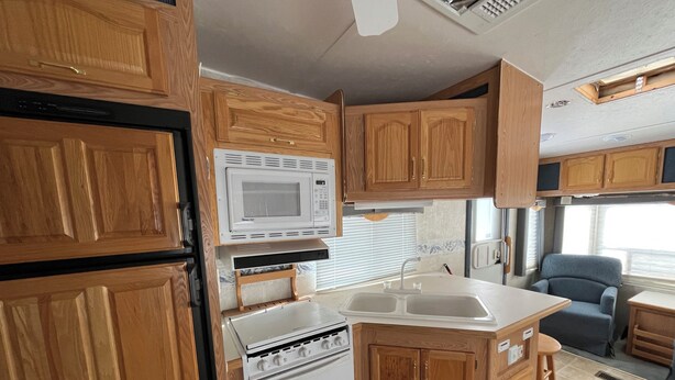 Une cuisine compacte pour camping-car, avec des placards en bois, un four à micro-ondes, une cuisinière et un évier.