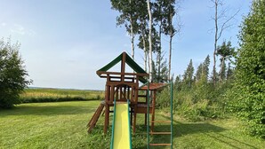 Une aire de jeux avec un toboggan et des structures d’escalade, située dans un espace verdoyant avec des arbres.