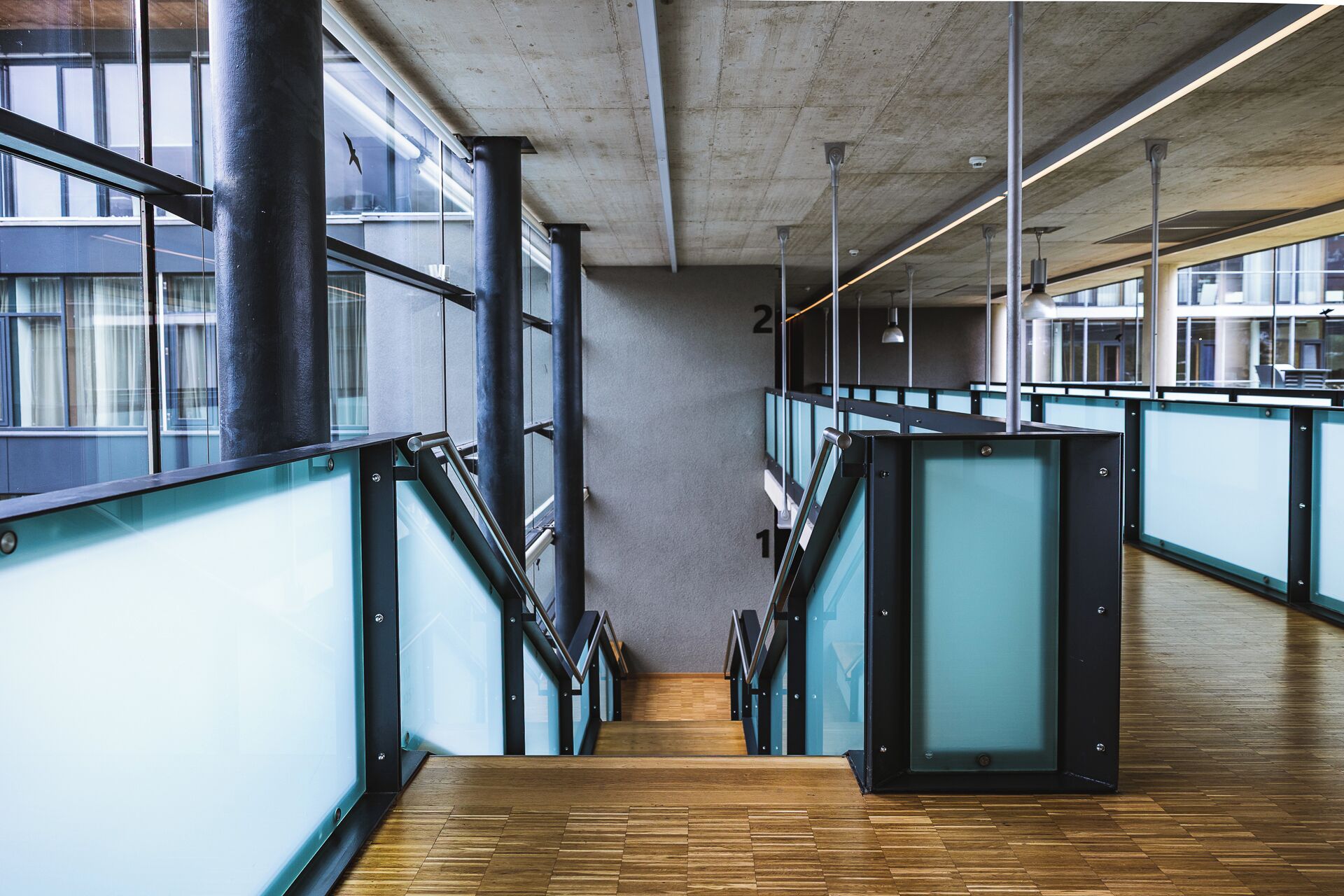 A modern interior with a staircase, glass partitions, and a concrete ceiling.