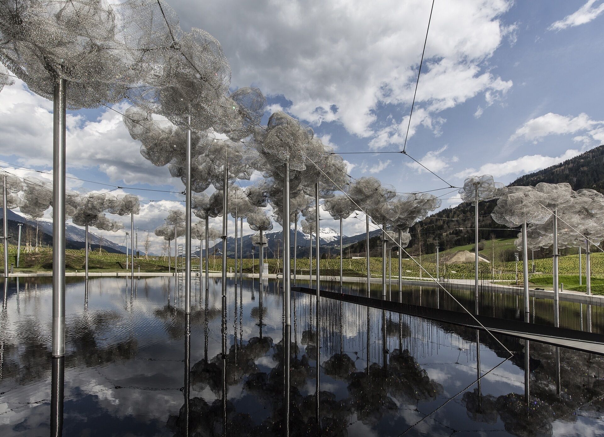 A serene outdoor setting with a reflective water body, metal poles, and a mountainous backdrop.