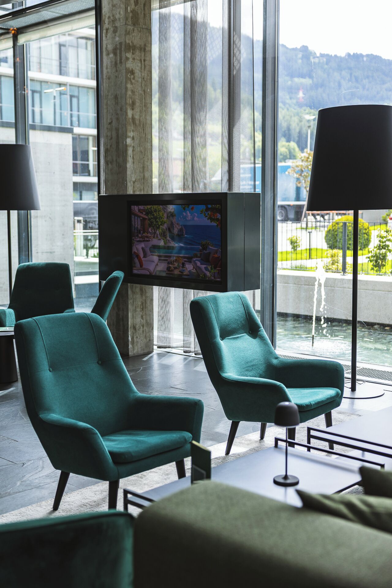Habitación moderna con dos sillones azul turquesa, un televisor de pantalla plana y un amplio ventanal con vistas al agua y vegetación.